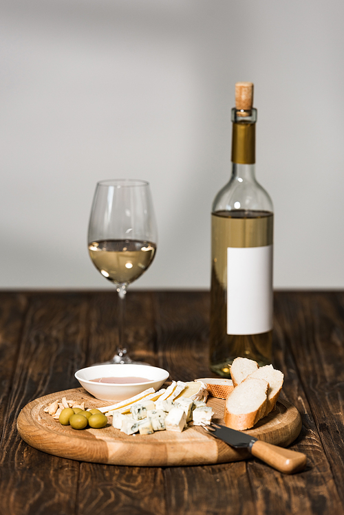 bottle of wine, wine glass, cheese, olives, sauce and bread on wooden surface