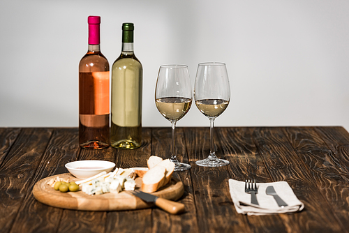 bottles of wine, wine glasses, cutlery, cheese, olives, sauce and bread on wooden surface