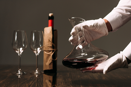 partial view of waiter in white gloves holding jug of wine in restaurant