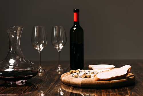 cheese, bread, sauce, bottle of wine, wine glasses and jug on wooden surface