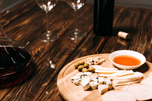 cheese, bread, sauce, bottle of wine, wine glasses and jug on wooden surface