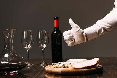 cropped view of waiter in white glove showing thumb up near table with food and wine
