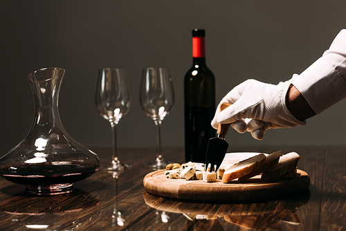 cropped view of waiter in white glove near table with food and wine