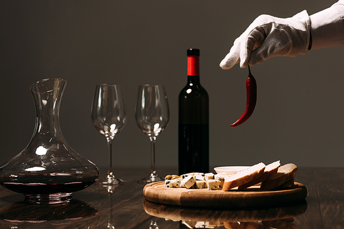 cropped view of waiter in white glove holding pepper near table with food and wine