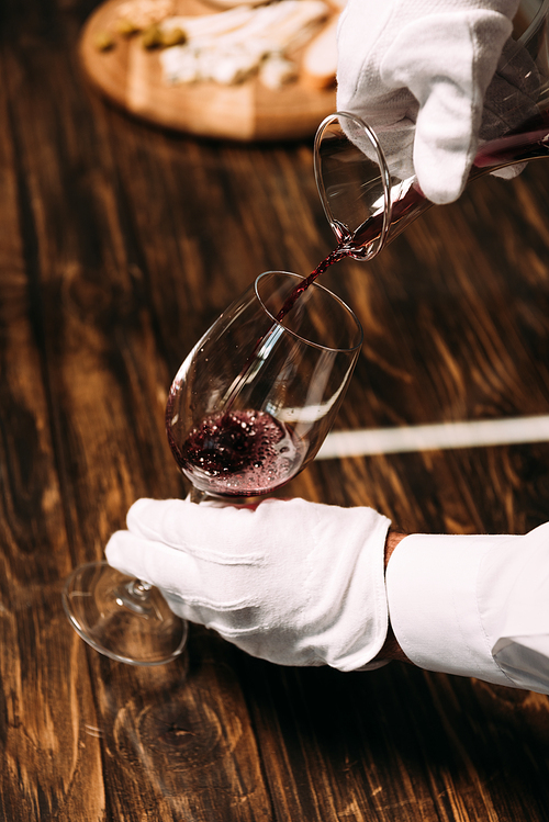 cropped view of waiter in white gloves pouring wine in wine glass