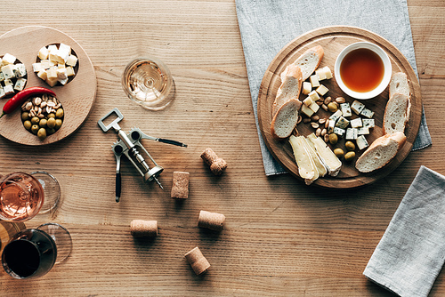 top view of wine glasses, food, corkscrew and corks on wooden surface