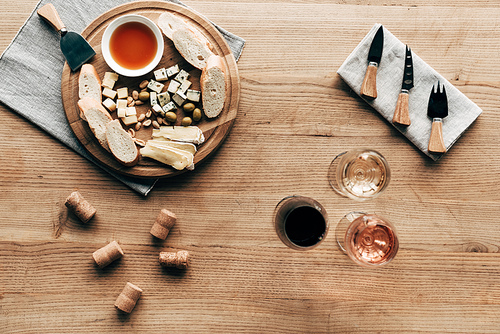 top view of wine glasses, sauce, bread, cheese, olives, corks and cooking utensils on wooden surface