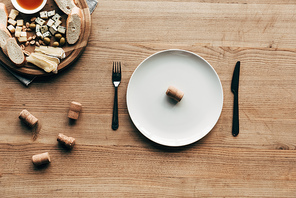 top view of plate with cork, cutlery and food on wooden table