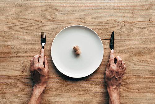 cropped view of man holding fork and knife at table with plate and cork