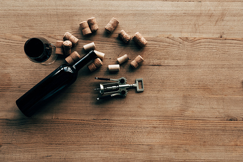 top view of bottle of wine, wine glass, corks and corkscrew on wooden surface