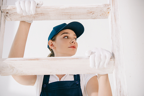 pretty young painter in uniform climbing on ladder and looking away