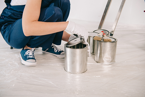 cropped view of young painter opening cans with paint