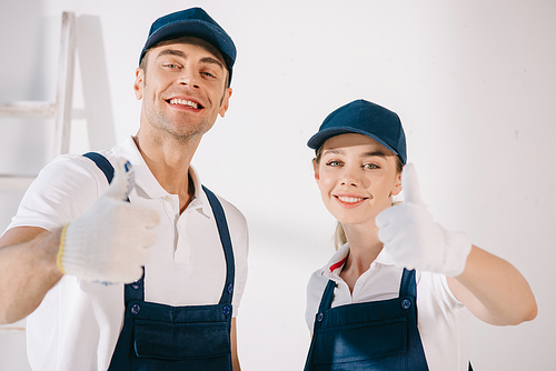 two cheerful painters showing thumbs up while smiling at camera