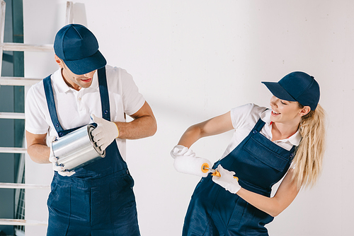 cheerful painters having fun while holding can with paint and paint roller