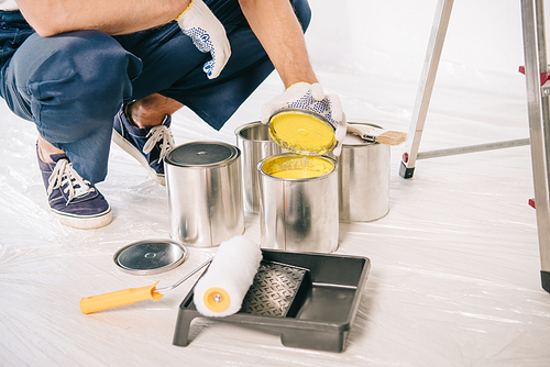 partial view of painter in uniform opening can with yellow paint