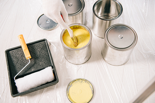 cropped view of man dipping paintbrush into can with yellow paint