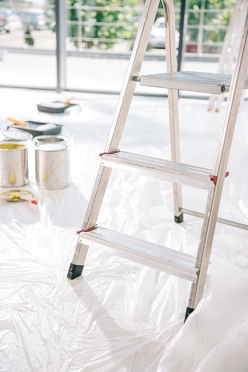 selective focus of ladder in room with cans of paint on white floor covered with cellophane