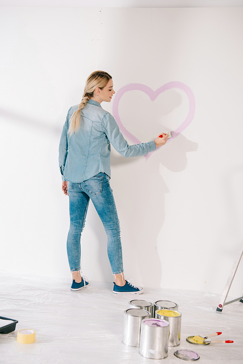 pretty young woman drawing heart with pink paint on white wall