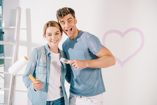 happy young couple  while holding pink paintbrush and paint roller