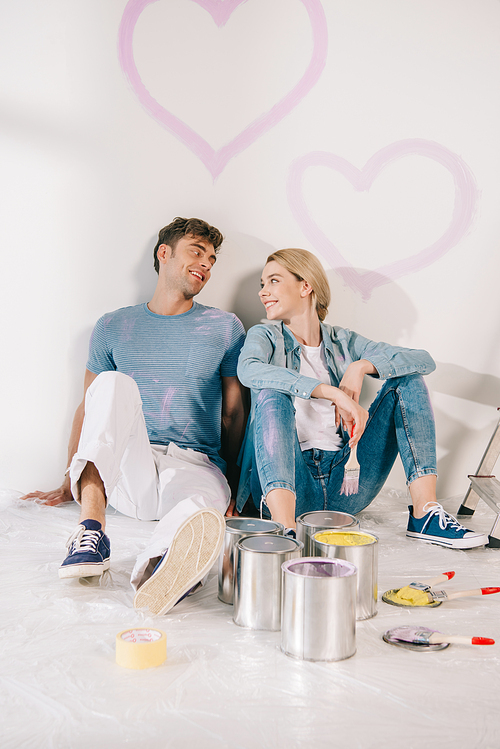 happy young couple sitting on floor by white wall under drawn pink hearts