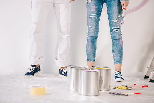 cropped view of man and woman standing by white wall near cans with paint