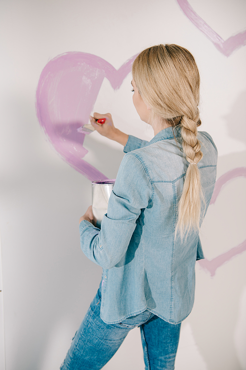 young woman drawing pink heart on wall with paintbrush