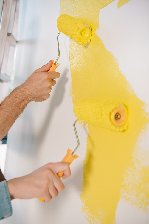 partial view of man and woman painting wall in yellow with paint rollers