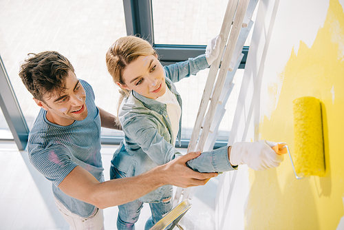 high angle view of handsome young man helping girlfriend painting wall in yellow