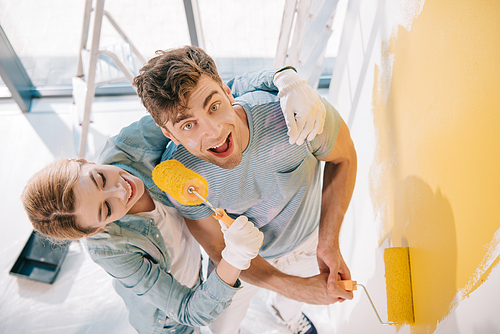 cheerful girl having fun while frightening boyfriend with paint roller