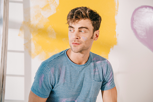 handsome young man looking away near white wall painted in yellow