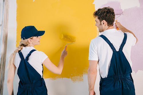 young painters in uniform looking at each other while painting wall in yellow and pink