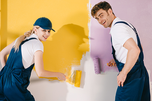 two cheerful painters  while painting wall in yellow and pink