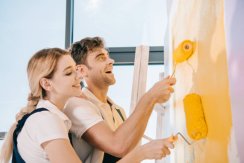 two young painters smiling while painting wall with paint rollers