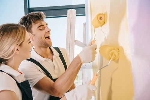 two young painters painting wall in yellow and pink with paint rollers