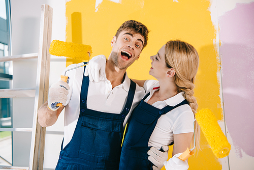 cheerful painter  while standing near attractive colleague