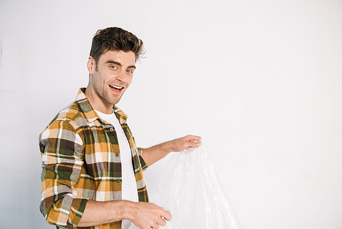 smiling young man holding cellophane while preparing for wall painting