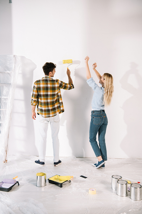 cheerful young woman dancing while boyfriend holding yellow paint roller