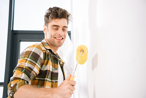 handsome young man smiling while holding yellow paint roller