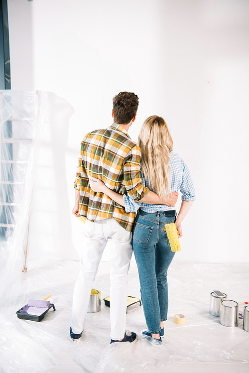 back view of young couple embracing while looking at white wall at home