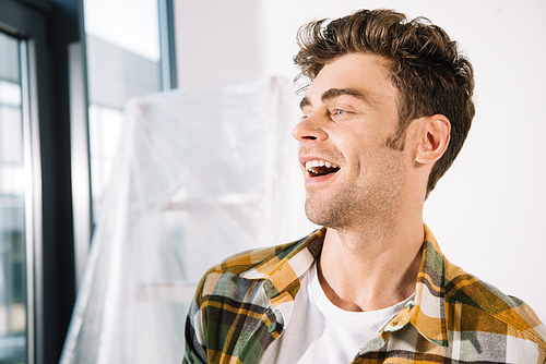 cheerful young man looking away while standing near ladder covered with cellophane