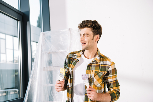 handsome young man looking away while holding yellow and pink paintbrushes