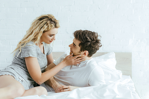 attractive blonde woman touching cheek of handsome man lying on bed