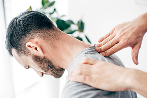 Cropped view of chiropractor massaging male patient neck in massage cabinet at clinic