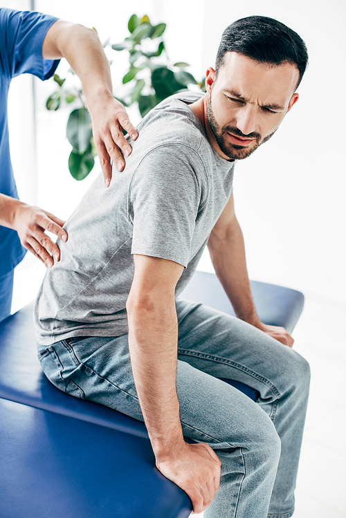 chiropractor massaging back of good-looking man in hospital