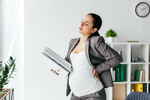 exhausted pregnant woman holding back and plenty of folders