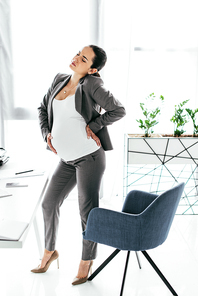 full length view of pregnant woman standing near office chair in office and enduring pain