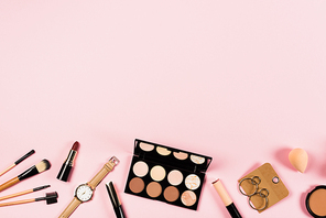 top view of wristwatch, earrings and decorative cosmetics on pink