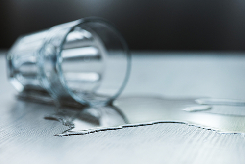 selective focus of glass with spilled water on textured wooden surface