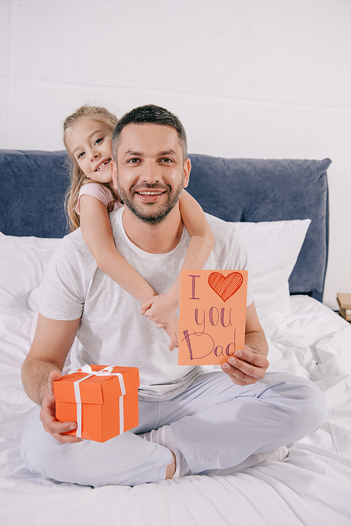 smiling child embracing happy dad holding gift box and fathers day greeting card