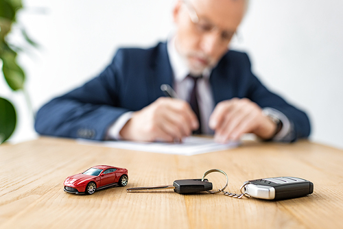 selective focus of toy car and car key near car dealer in office